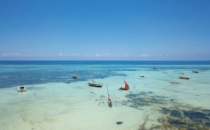 Un paysage côtier avec des bateaux ancrés dans des eaux peu profondes, un ciel dégagé et une mer calme.