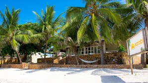 Een hotel aan het strand met palmbomen, een hangmat en een bord.
