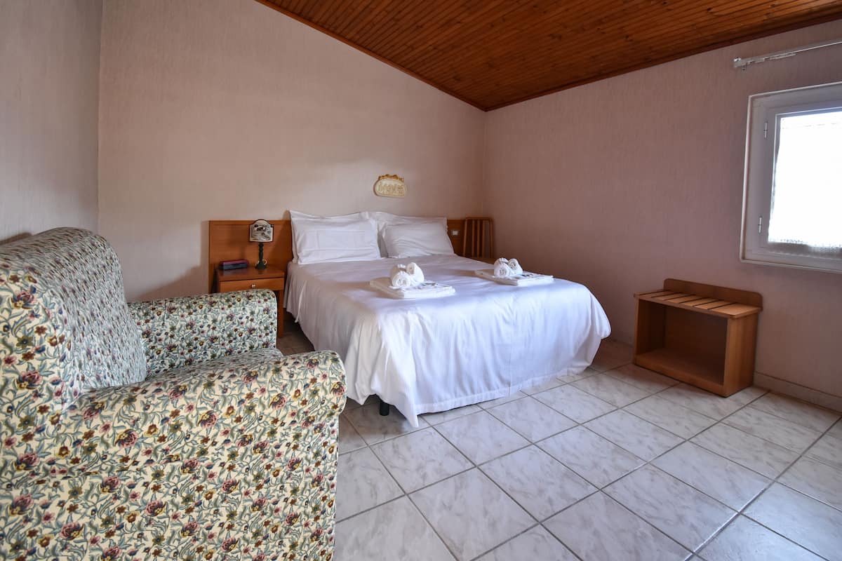 A bedroom with a bed, a floral-patterned sofa, a wooden nightstand, and a small wooden shelf.