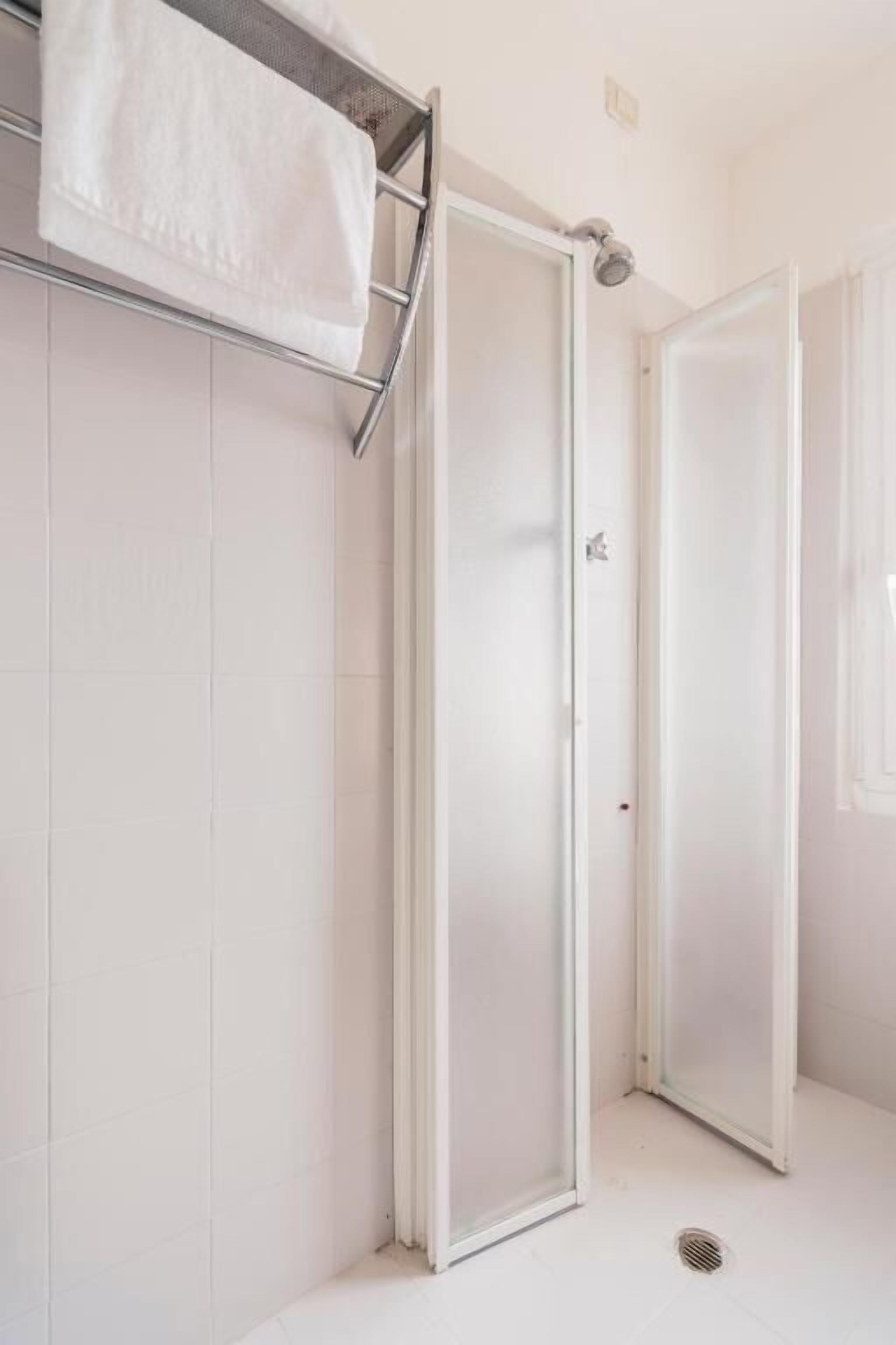 Un baño con paredes de azulejos blancos, una ducha con puerta de cristal y un perchero.