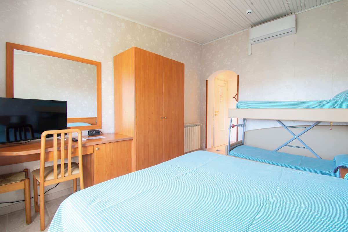 A room with a bunk bed, a desk with a chair, a television, and a wardrobe.