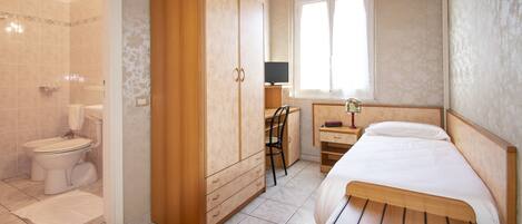 A bedroom with a wooden bed, a desk with a chair, a wardrobe, and a shower area.