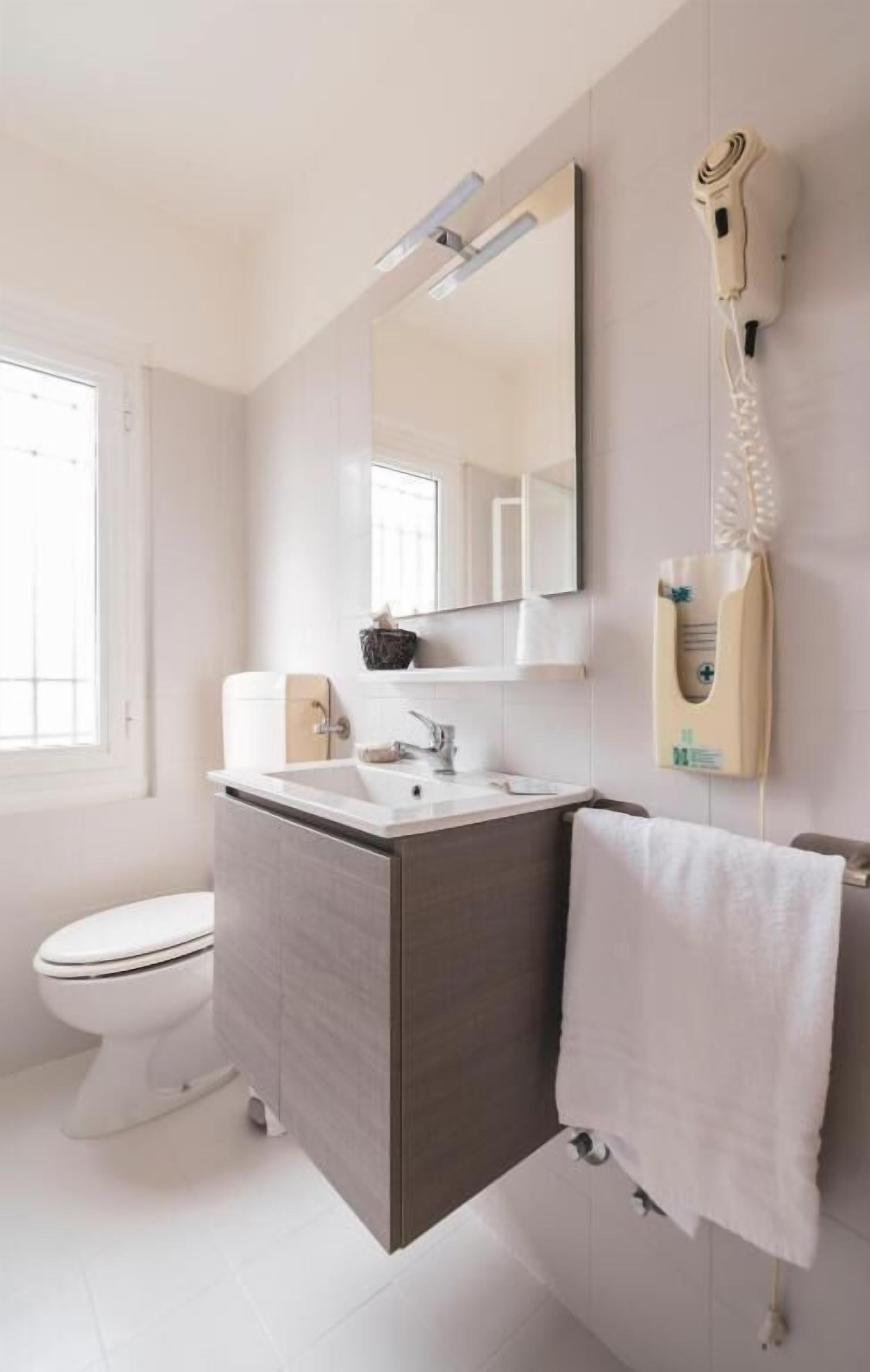 A bathroom with a toilet, sink, mirror, towel rack, and a hairdryer mounted on the wall.