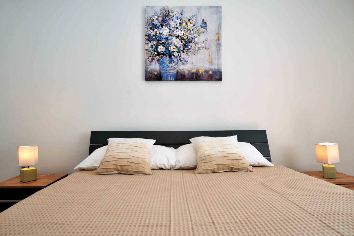 A bedroom with a large bed, two bedside tables with lamps, and a wall-mounted painting.