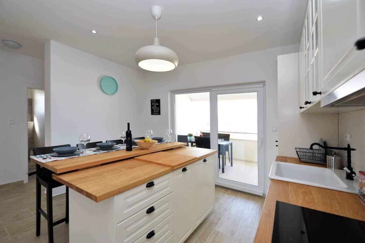 A modern kitchen with a wooden island, white cabinets, and a large window.
