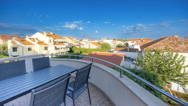 Un balcón con mesa y sillas, con vistas a una zona residencial con casas.