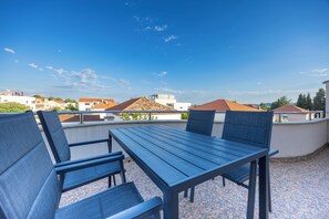 A rooftop terrace with a table and chairs, a clear sky, and surrounding buildings.