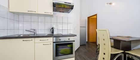 Une cuisine moderne avec des armoires blanches, un four encastré, une hotte de cuisinière en acier inoxydable et un coin repas avec une table et des chaises.