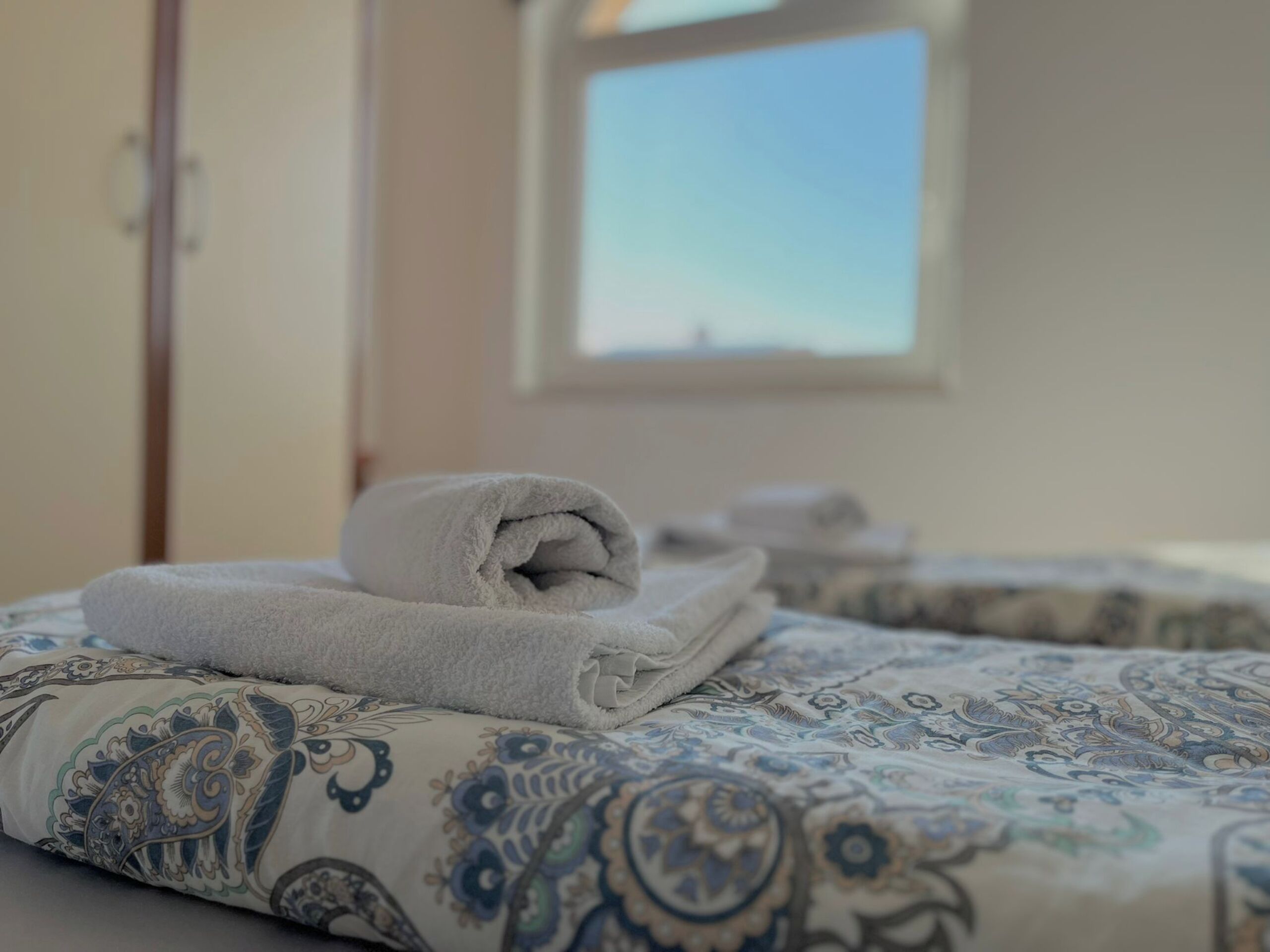 Una cama bien hecha con una colcha estampada y una toalla blanca enrollada.