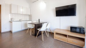 Una cocina moderna con armarios blancos, una mesa de comedor con sillas, un televisor de pantalla plana y un microondas.