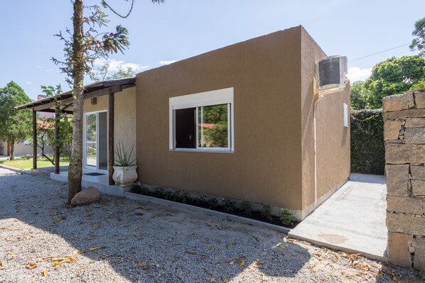 A modern house with a beige exterior, a small window, and a stone wall. - Cabanas Canasvieiras (Florianópolis)