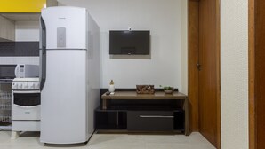 Een compacte keuken met een witte koelkast, een fornuis en een magnetron. Een flatscreen-tv is aan de muur bevestigd boven een houten aanrecht met een plant en decoratieve objecten.