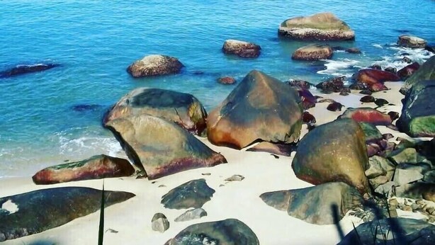 Una playa con grandes rocas y agua azul cristalina.