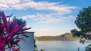 Un patio frente al lago con asientos y plantas, con vistas a un lago tranquilo y colinas lejanas.