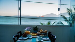 Una mesa de comedor dispuesta con alimentos para el desayuno y vista al océano.