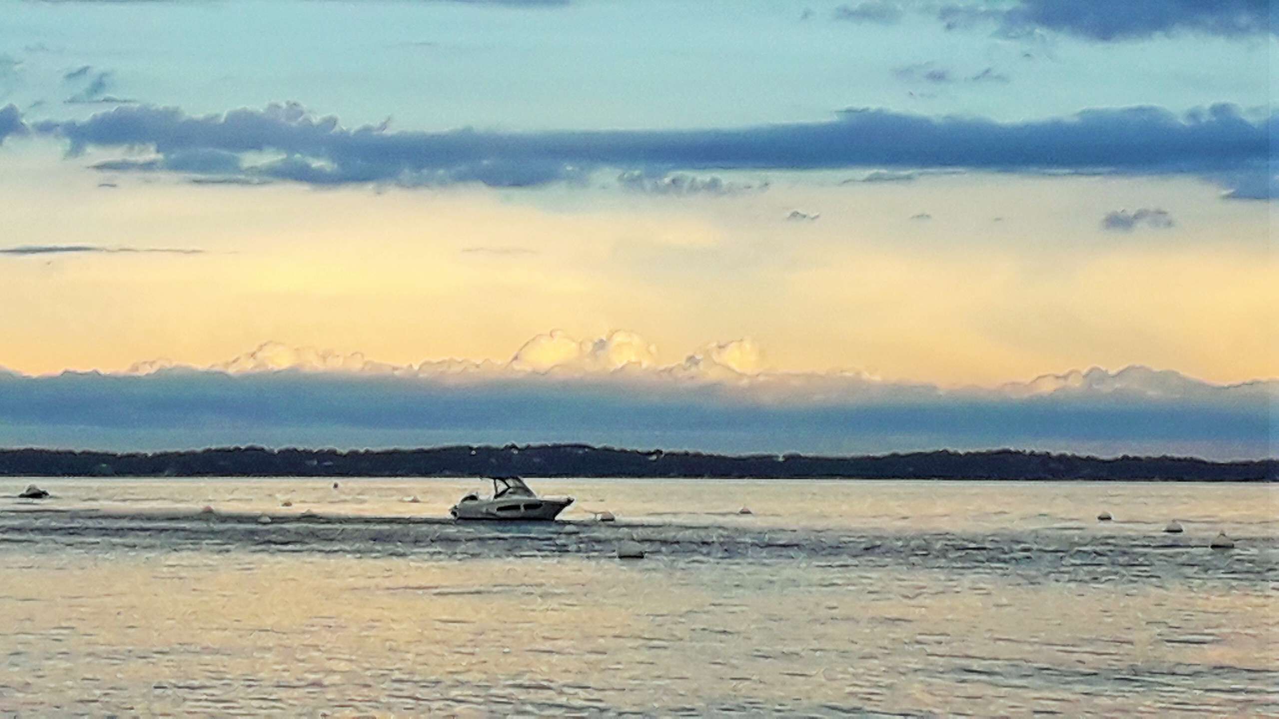 Un bote sobre aguas tranquilas, con una orilla lejana y cielo nublado.