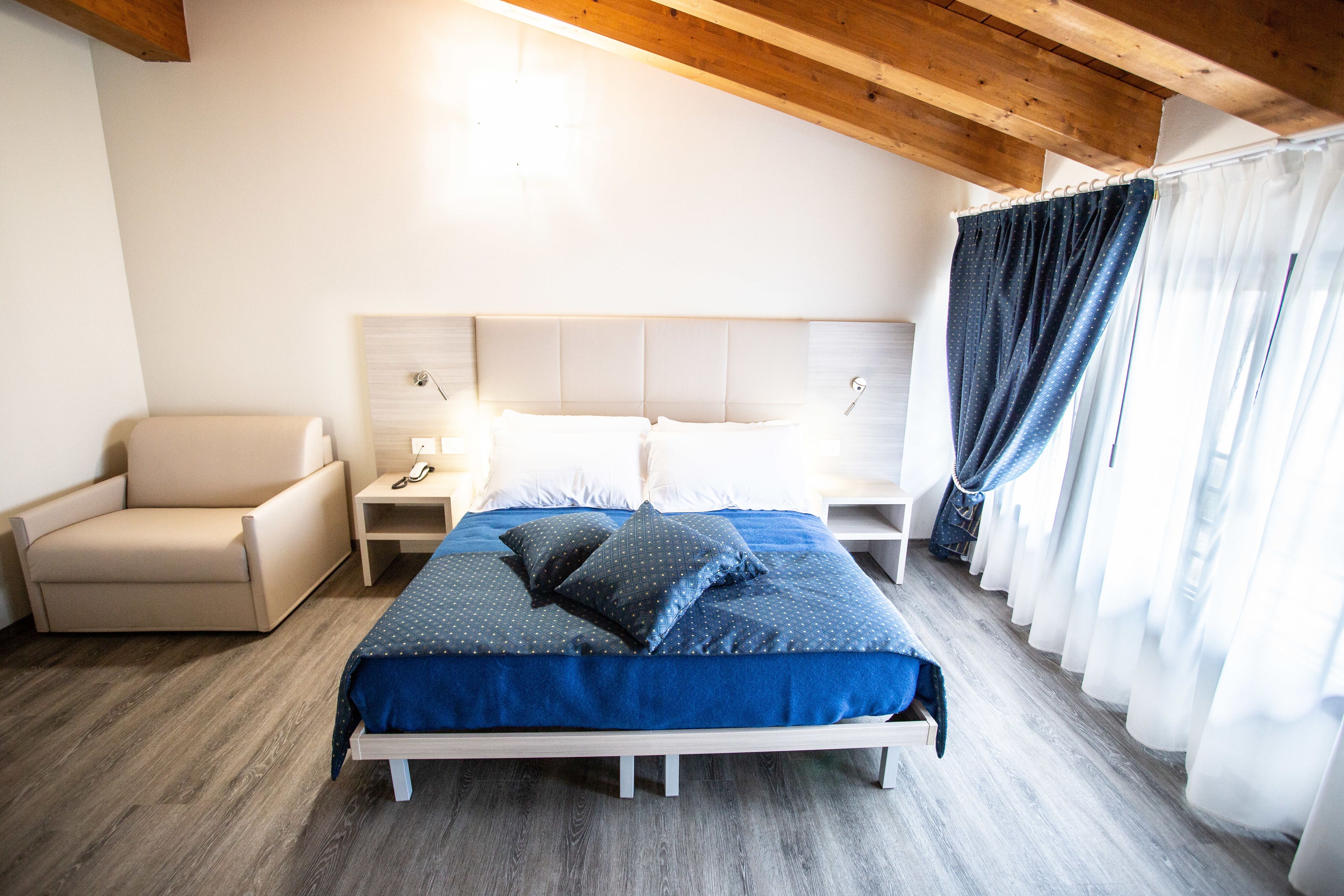 A bedroom with a bed, a chair, a nightstand, and a window with curtains.