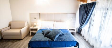 A bedroom with a bed, a chair, a nightstand, and a window with curtains.