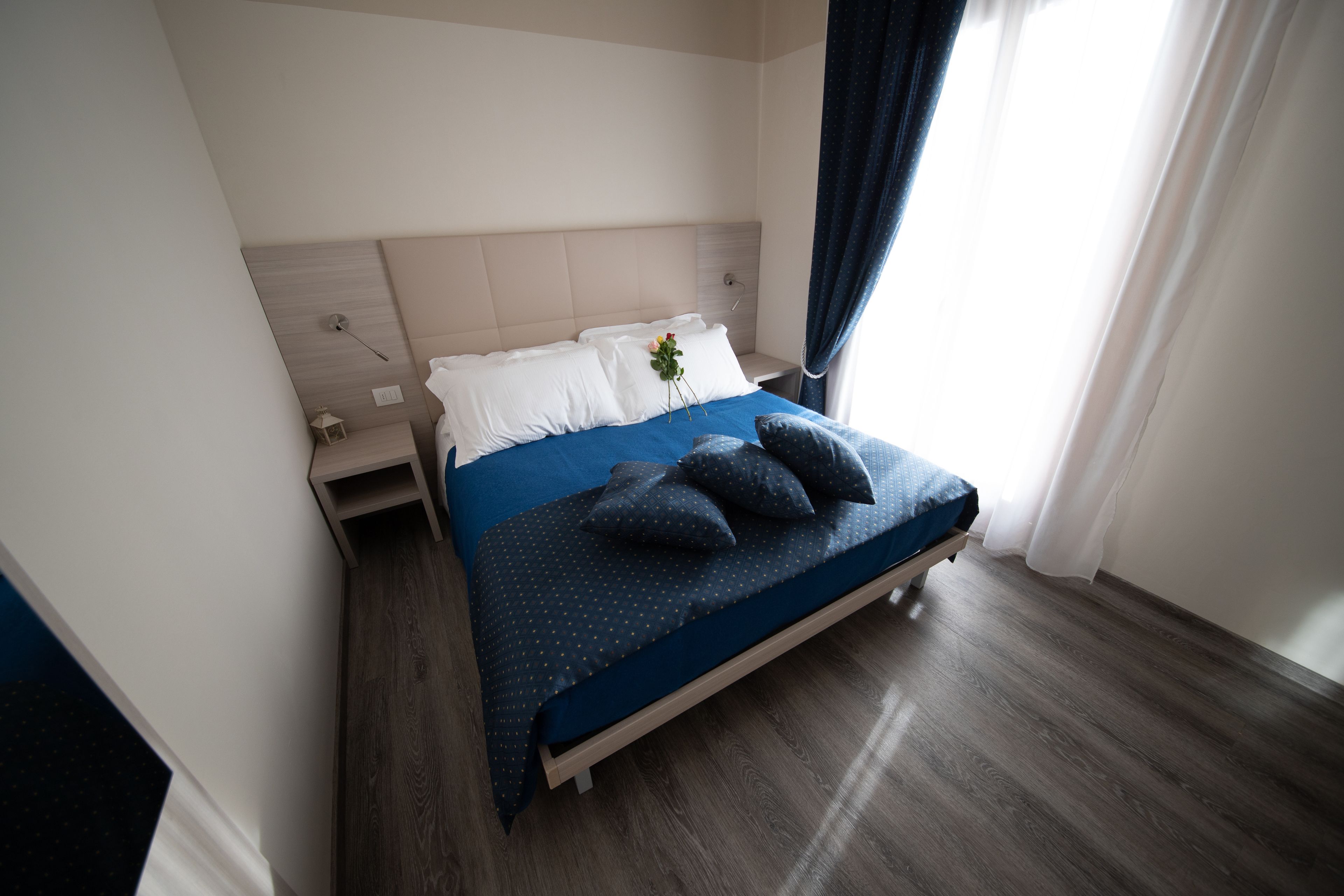 A modern hotel room with a bed, wooden flooring, and a nightstand.