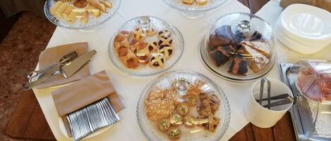Una mesa con diferentes alimentos cubiertos por campanas de cristal, acompañada de cubiertos y servilletas.