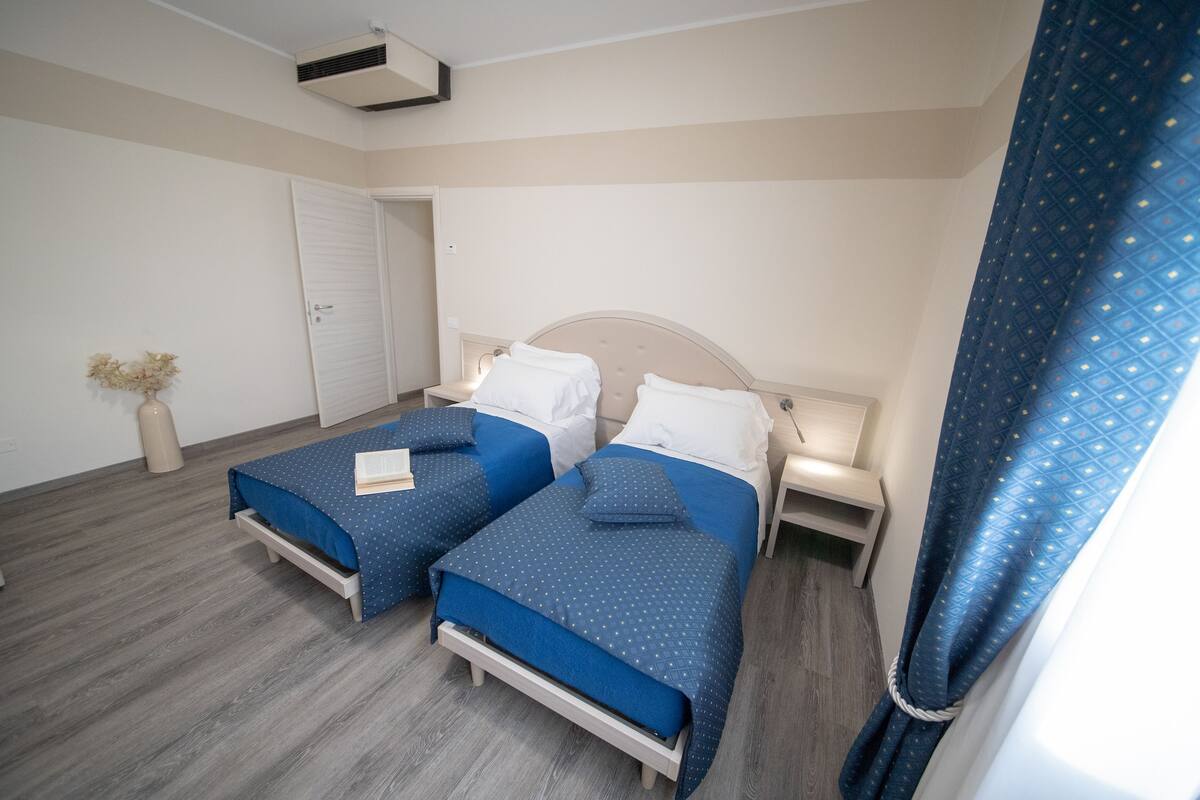 Une chambre avec deux lits, une armoire et une table de chevet avec une lampe.