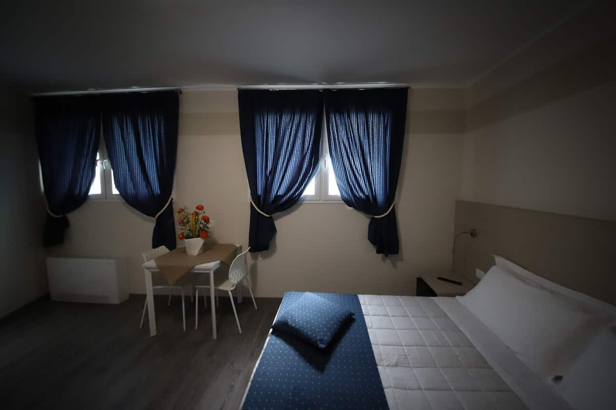 Une chambre à coucher avec un lit, un bureau et deux fenêtres avec des rideaux.