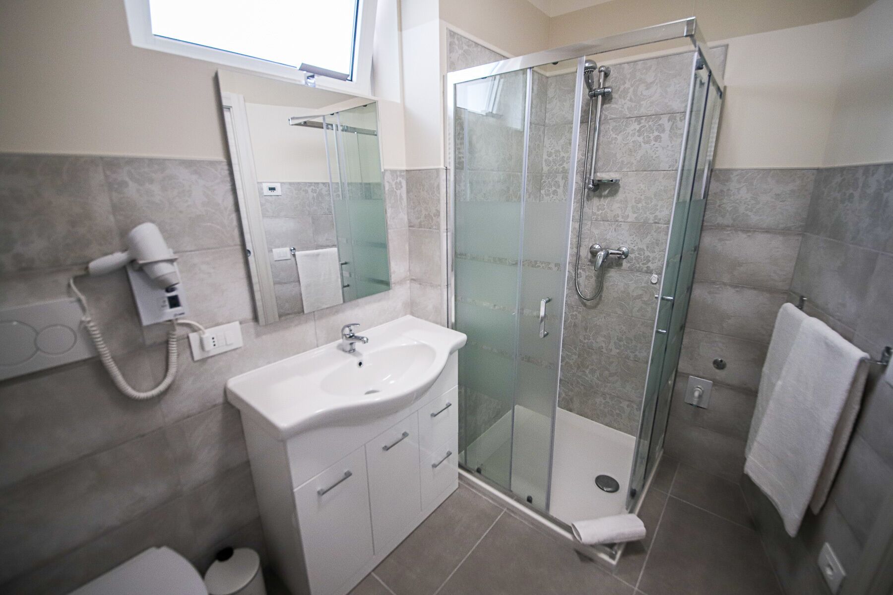 Une salle de bain moderne avec une douche à parois de verre, un lavabo blanc et un sèche-cheveux.