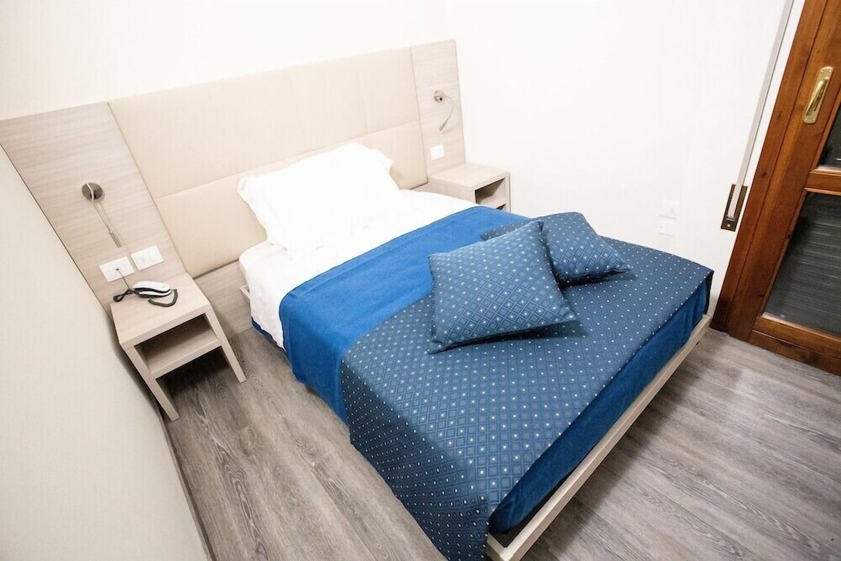 Un lit avec une couvre-lit bleue et des oreillers, une table de chevet en bois avec un téléphone, et un plancher en bois.