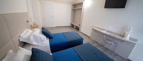 A hotel room with two beds, a TV, a wardrobe, and a desk with a lamp.