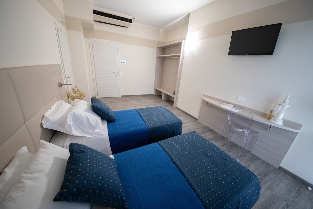 Une chambre d’hôtel avec deux lits, une télévision, une armoire et un bureau avec une lampe.
