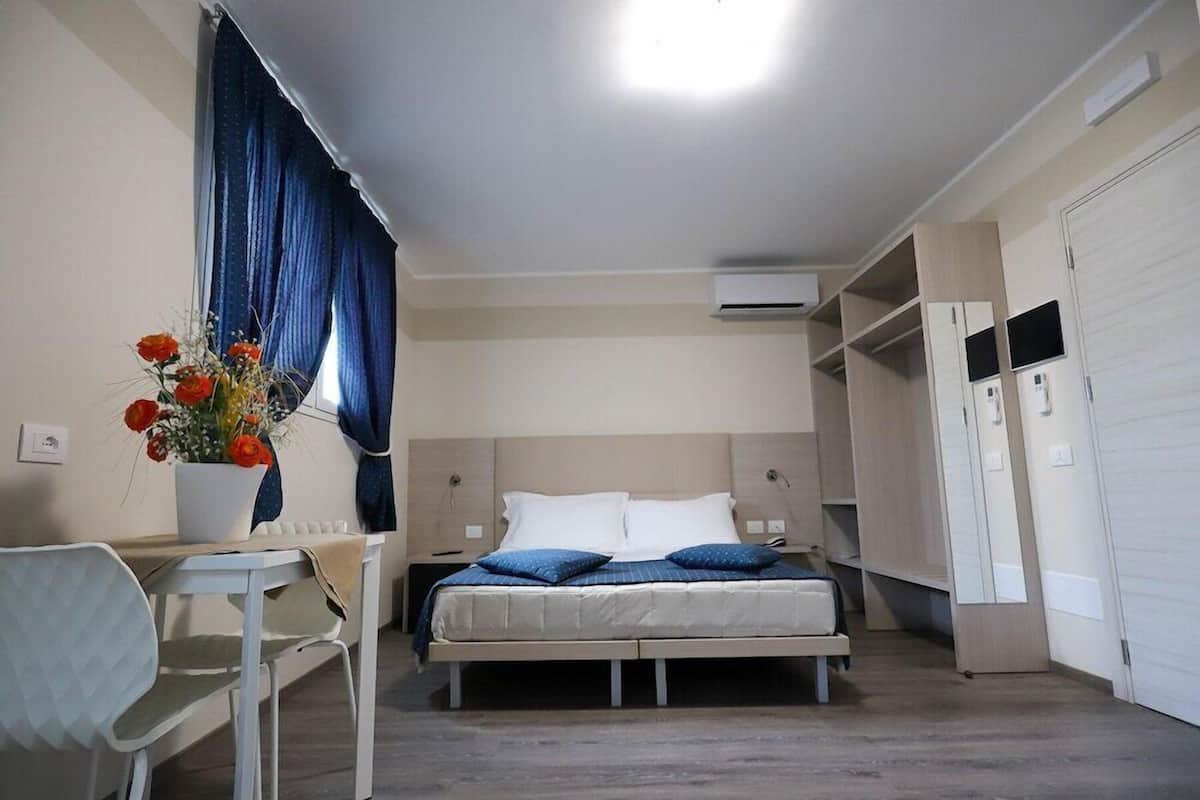 Une chambre à coucher comprenant un lit, des tables de chevet, une chaise, un bureau, une plante en pot et une armoire.
