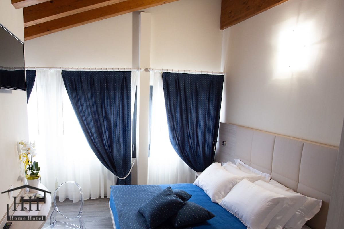 Une chambre à coucher avec un lit, des rideaux, une table de chevet et une petite plante en pot.