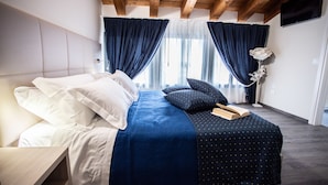 Ein Schlafzimmer mit Bett, Nachttisch, Wand-Fernseher und einem Fenster mit Vorhängen.