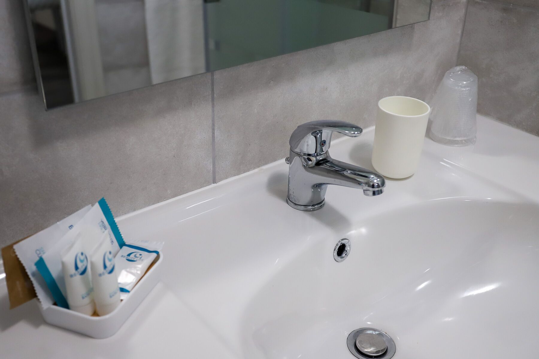 A bathroom sink with a chrome faucet, a cup, and a dispenser with toiletries.