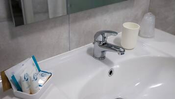 A bathroom sink with a chrome faucet, a cup, and a dispenser with toiletries.