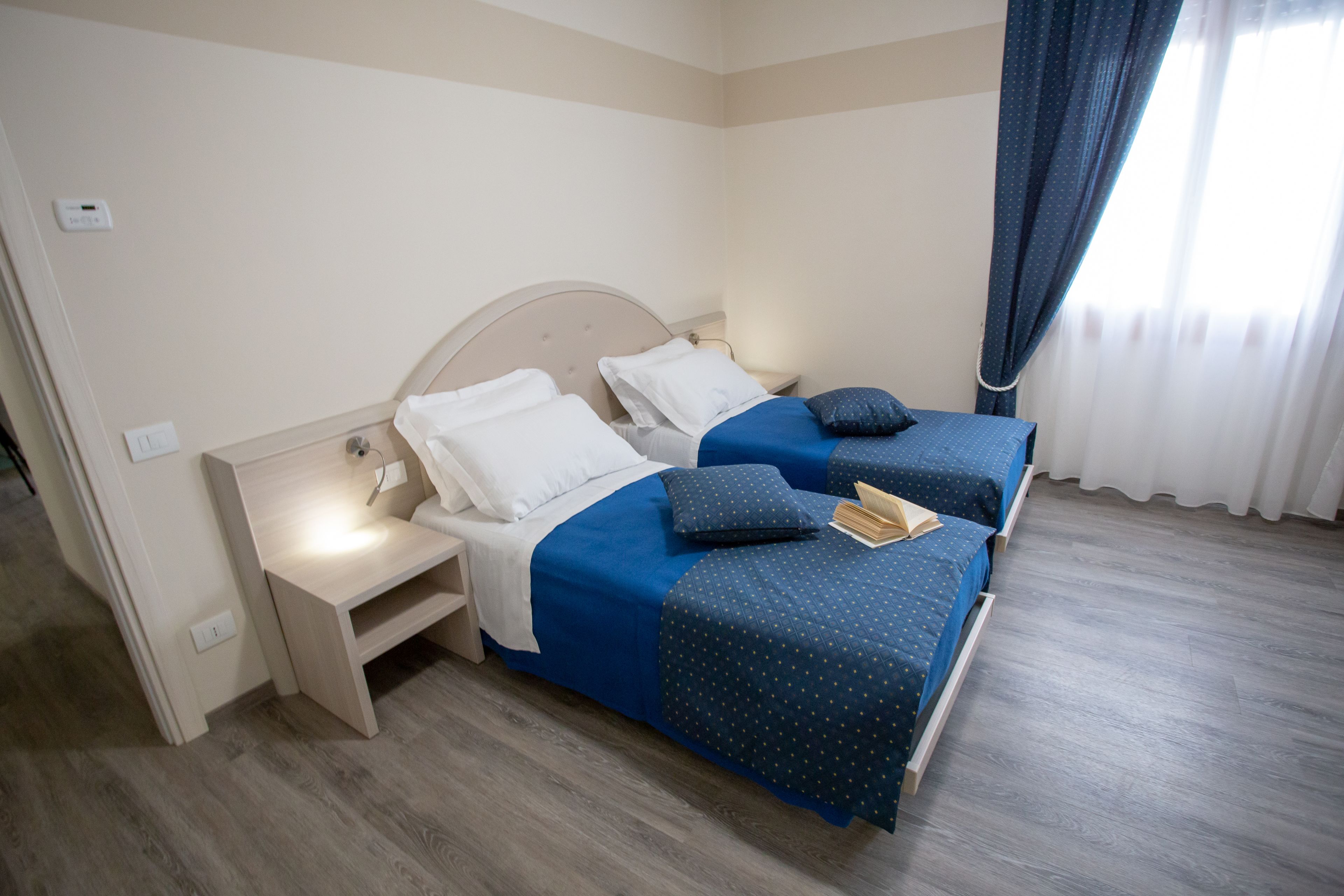 Una habitación de hotel con dos camas, una mesita de noche y una ventana con cortinas.