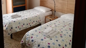A hotel room with two single beds, a wooden headboard, a small bedside table, a hanging plant, and a door with a glass panel. - B&B Vanvitelli (Caserta)