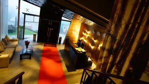 A modern lobby with a red carpet, a reception desk, a sofa, and a view of the outdoors. - Horton Towers & Cottages (Nuwara Eliya)
