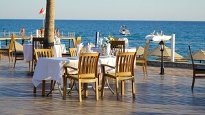 Un restaurante frente al mar con terraza, palmeras y vistas al océano.