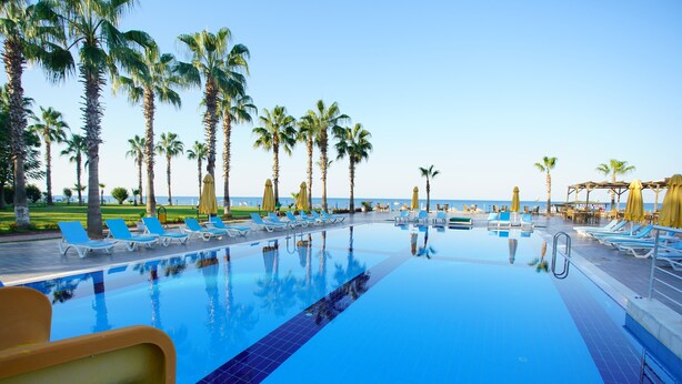 Zona de piscina con sillones de playa y sombrillas, rodeada de palmeras y vista al océano.