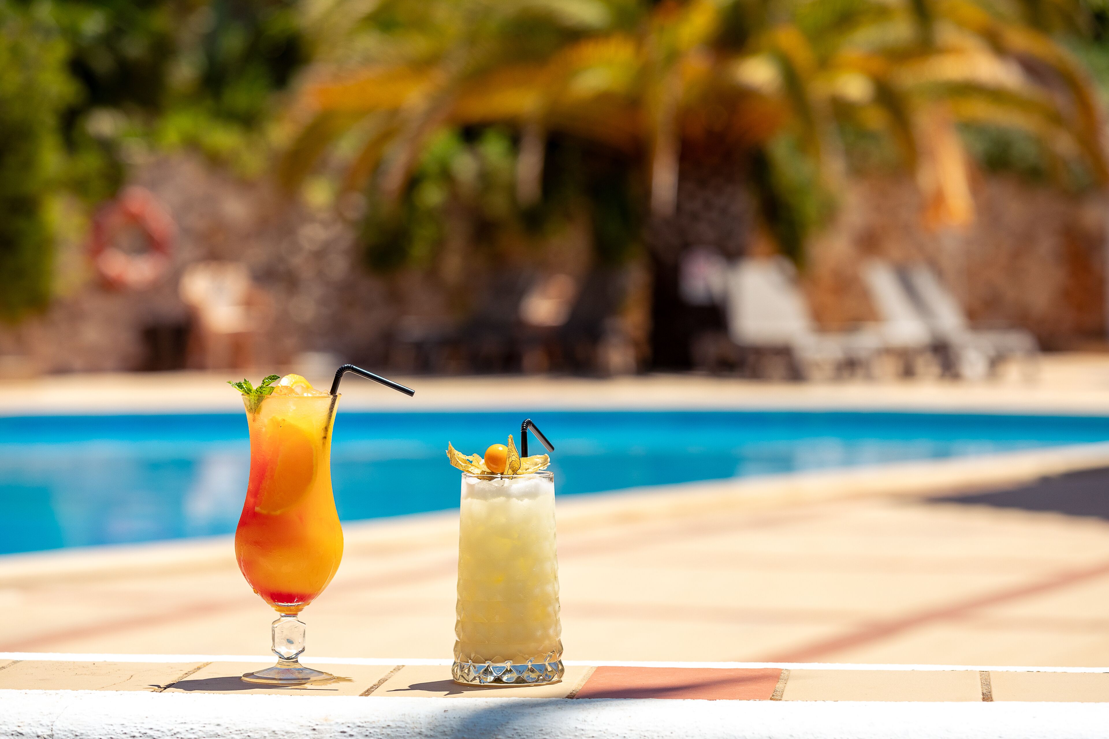 Deux cocktails sur une table au bord de la piscine, avec une piscine et des palmiers en arrière-plan.