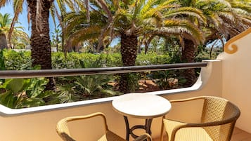 Un balcón con sillones de mimbre, una mesita redonda y vistas a palmeras y vegetación.