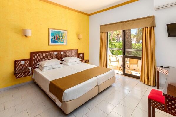 Une chambre d’hôtel avec un grand lit, un tableau au mur et un balcon avec des rideaux jaunes.