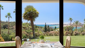 A dining table set with plates, glasses, and cutlery, overlooking a scenic view of a coastal landscape with palm trees and a clear sky. - Hotel Casabela (Lagoa)