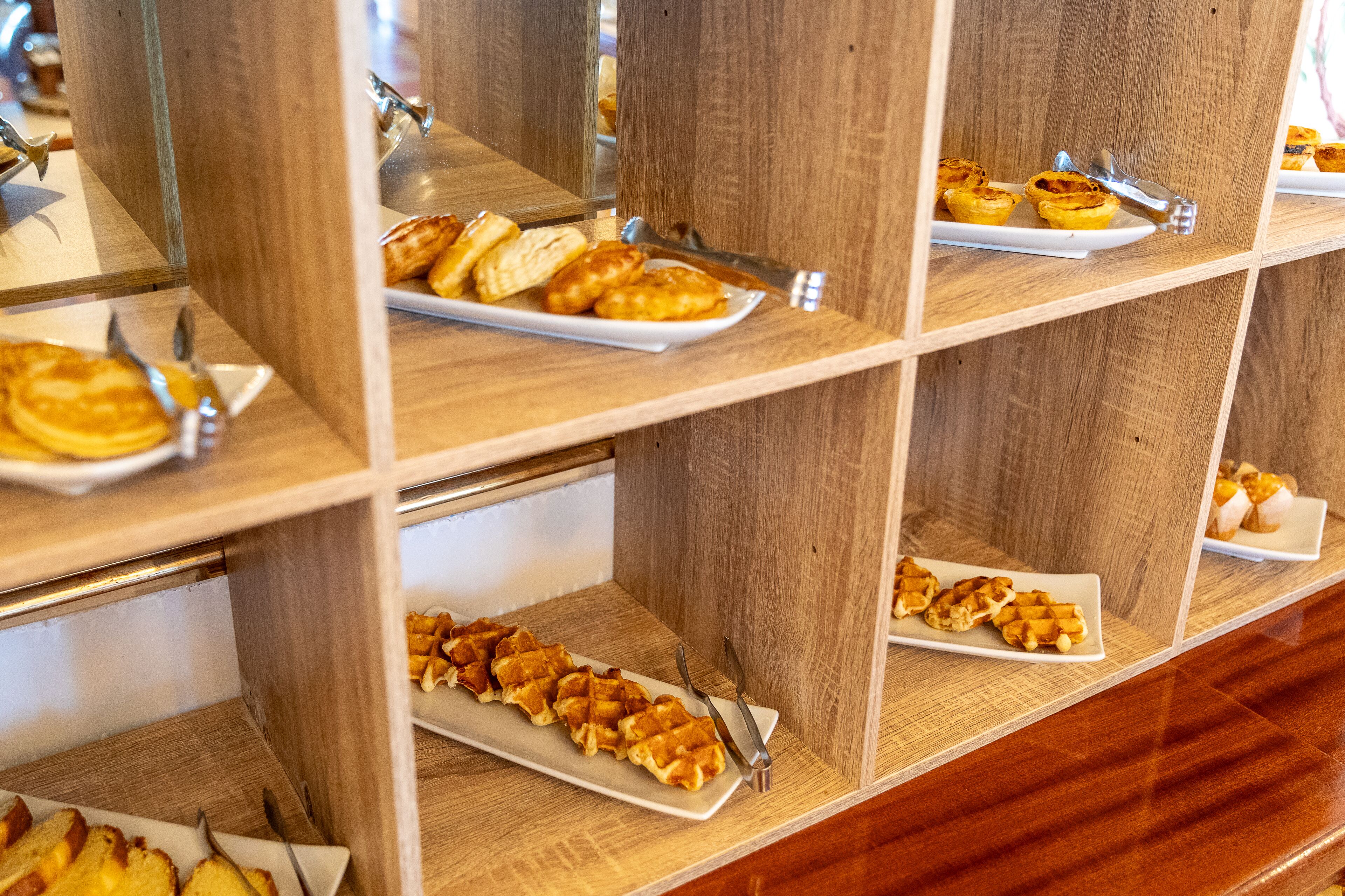 A buffet with various pastries and waffles on display.