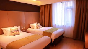Hotellihuone, jossa on kaksi sänkyä, puulattia ja suuri ikkuna, jossa on verhot.
