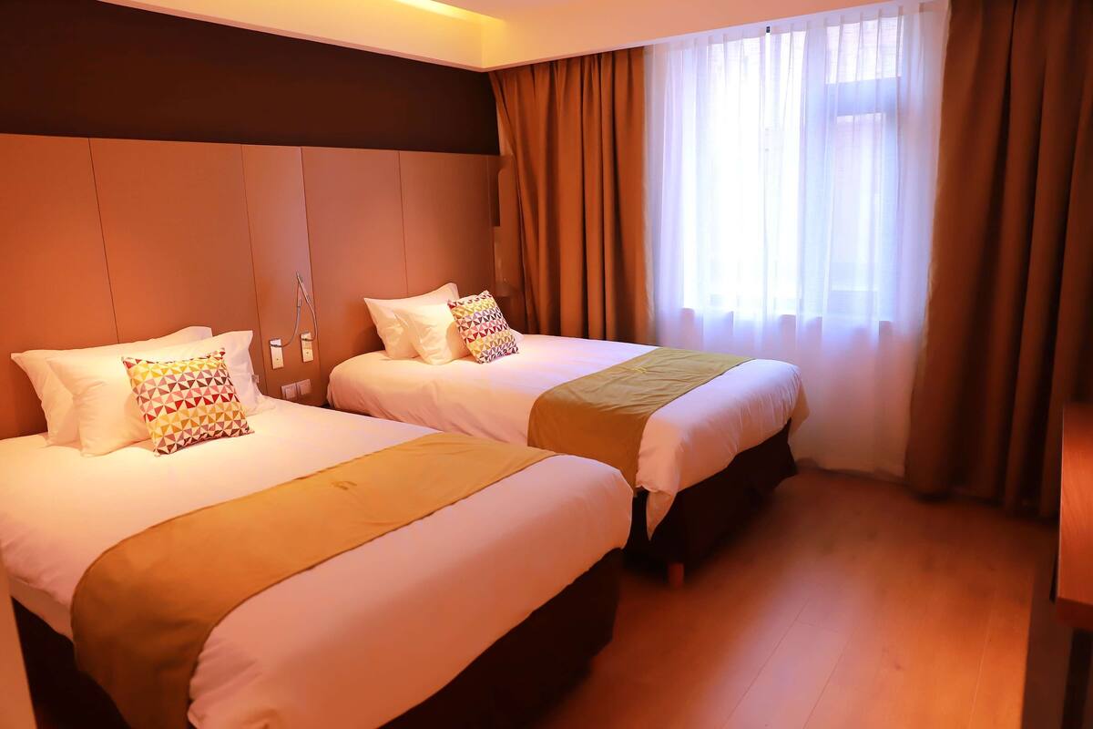 Habitación de hotel con dos camas, suelo de madera y un ventanal con cortinas.