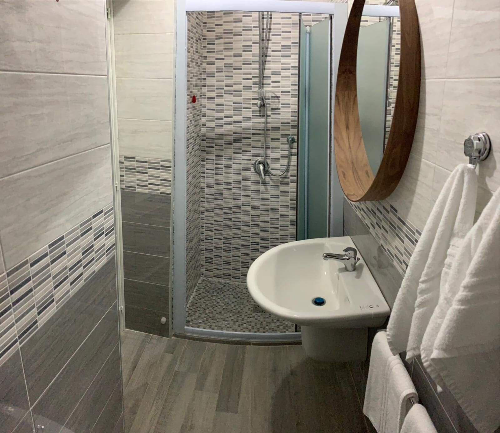 A modern bathroom with a glass-enclosed shower, a white sink, and a wooden-framed mirror.