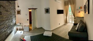 A room with a brick wall, a bed, a sofa, a TV, and a door leading to another room. - Franz Guest House (Naples)