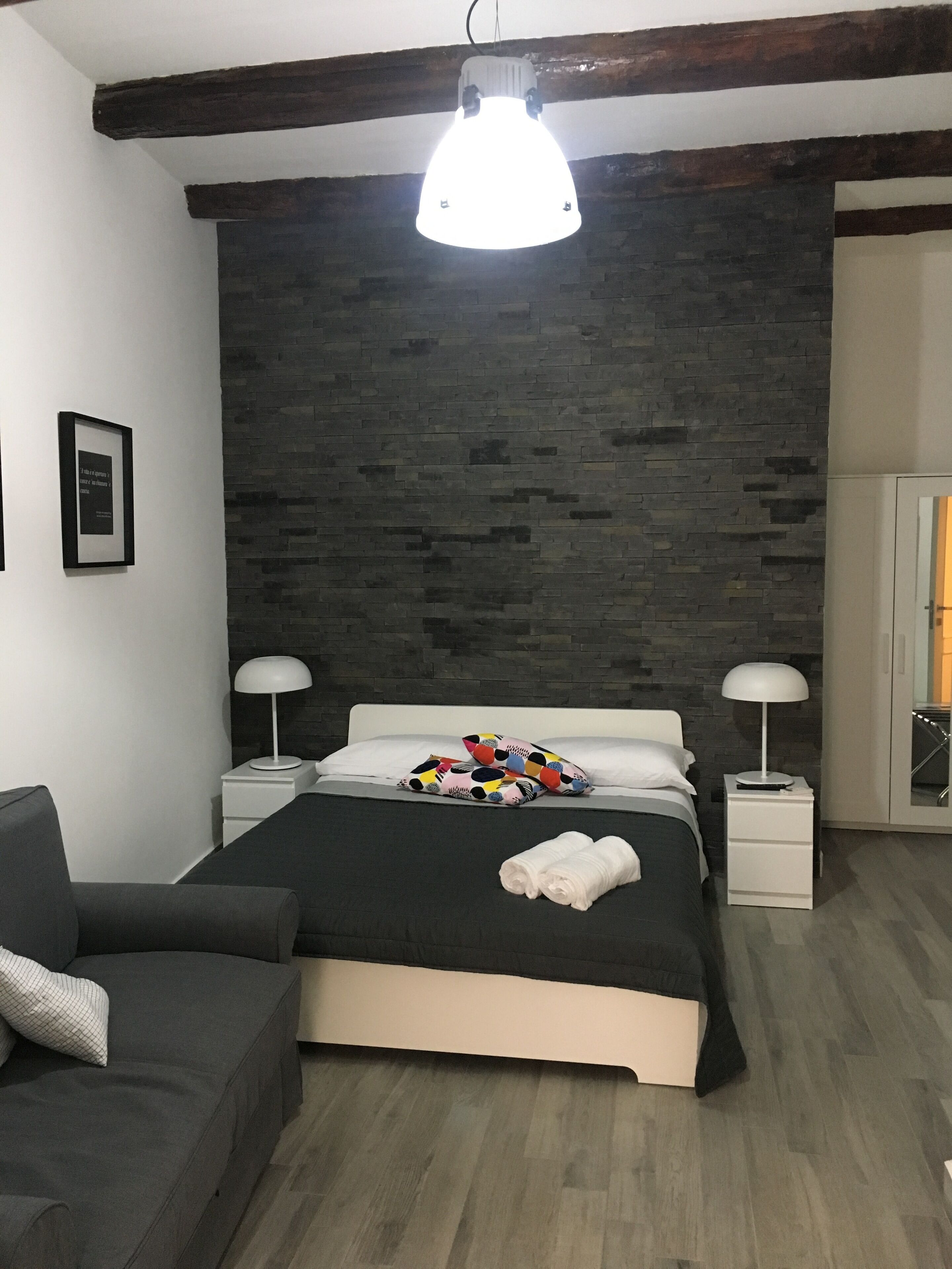 A modern bedroom with a bed, two bedside tables, a nightstand, a sofa, and a large window.
